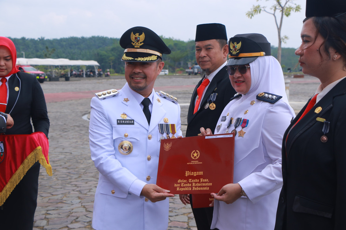 Pj Wali Kota Pekanbaru Risnandar Mahiwa Menyerahkan Piagam dan Pin Satya Lencana Karya Satya (SLKS) kepada Camat Rumbai Vemi Herliza Sebagai Salah Seorang Perwakilan ASN yang Menerima SLKS XX Tahun