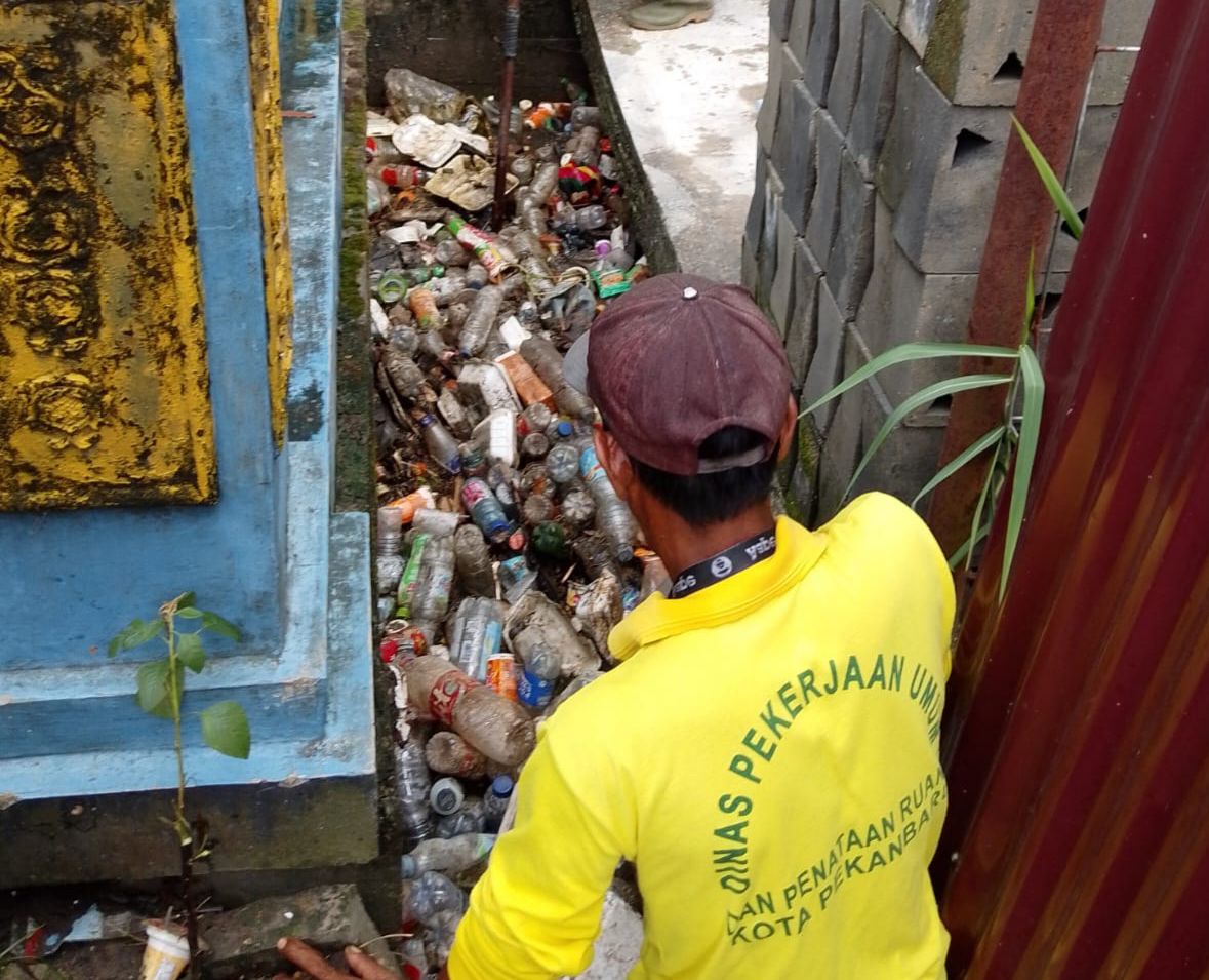 Pasukan kuning PUPR Pekanbaru, mengeruk sampah-sampah plastik dan makanan yang menyumbat drainase jalan